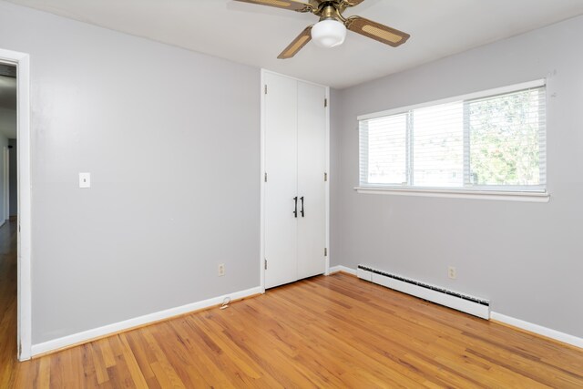 unfurnished bedroom featuring multiple windows, baseboard heating, light wood-type flooring, and ceiling fan