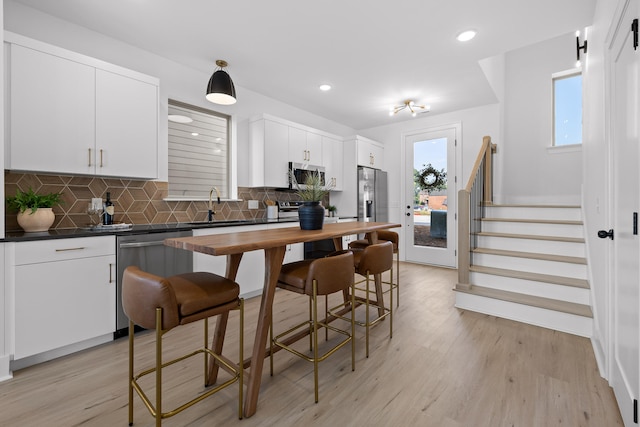 kitchen with stainless steel appliances, a healthy amount of sunlight, white cabinetry, and light hardwood / wood-style flooring