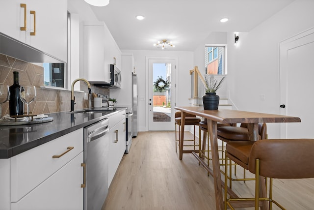 kitchen featuring stainless steel appliances, white cabinets, decorative backsplash, sink, and light wood-type flooring