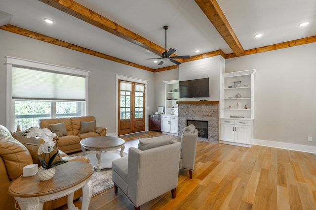 living room featuring a fireplace, beam ceiling, light wood-type flooring, and ceiling fan