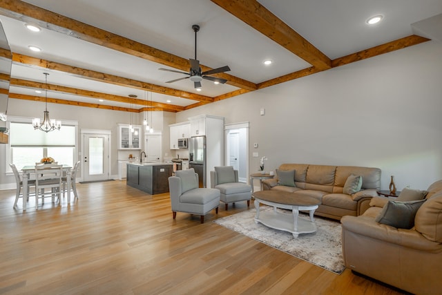 living room featuring sink, beam ceiling, light hardwood / wood-style flooring, and ceiling fan with notable chandelier