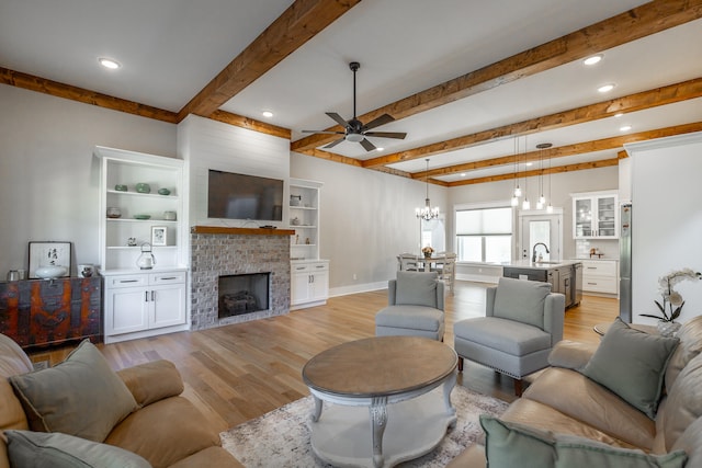 living room featuring beamed ceiling, sink, light wood-type flooring, and a brick fireplace