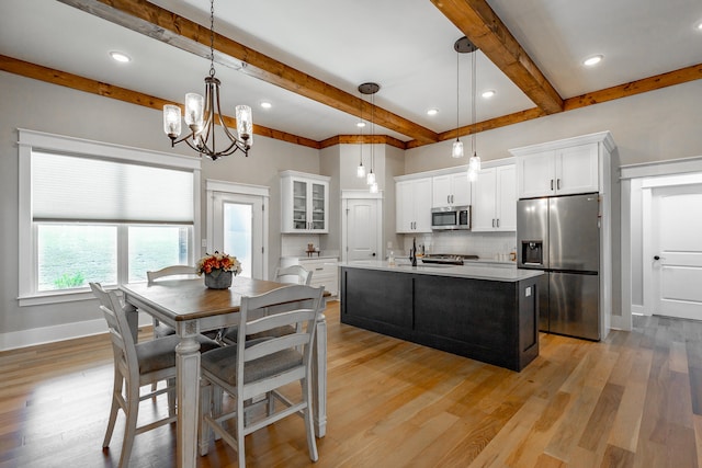 kitchen featuring a kitchen island with sink, appliances with stainless steel finishes, decorative light fixtures, and white cabinets