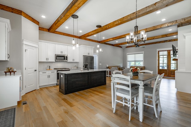 kitchen with white cabinetry, decorative light fixtures, stainless steel appliances, and an island with sink