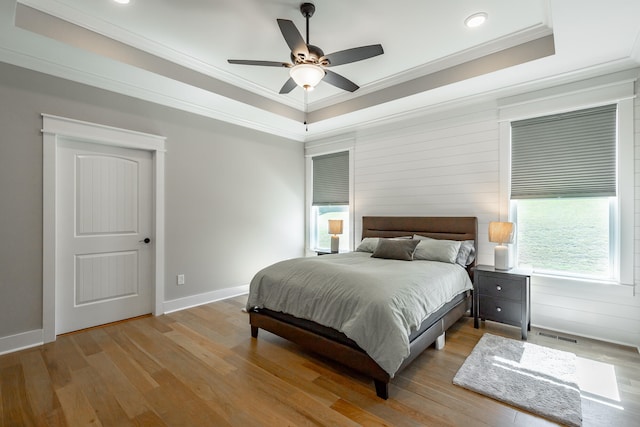 bedroom featuring light hardwood / wood-style flooring, ornamental molding, a tray ceiling, and ceiling fan