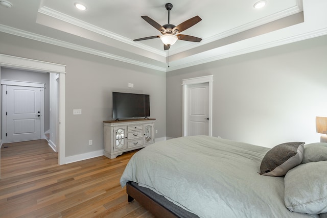 bedroom with crown molding, hardwood / wood-style flooring, a tray ceiling, and ceiling fan