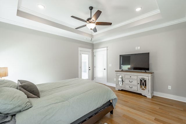 bedroom featuring crown molding, a tray ceiling, light wood-type flooring, and ceiling fan