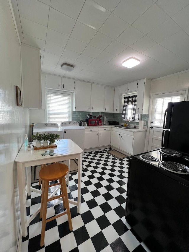 kitchen with white cabinets, black appliances, separate washer and dryer, and a healthy amount of sunlight