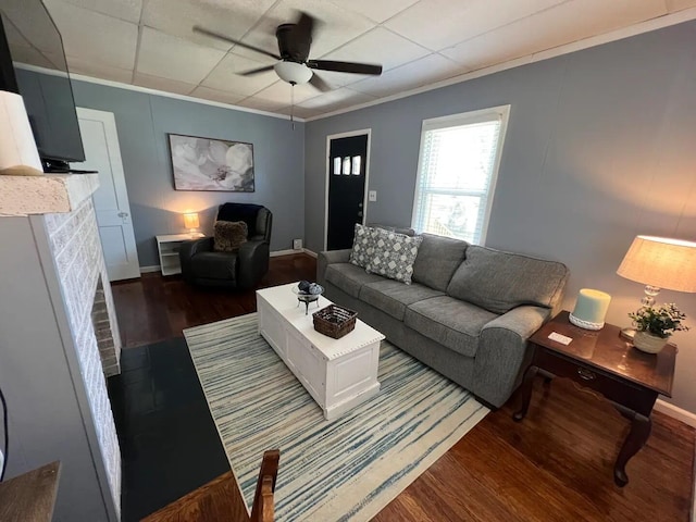 living room featuring a brick fireplace, dark hardwood / wood-style floors, crown molding, and ceiling fan