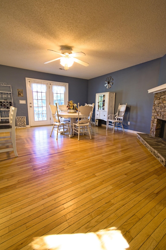 dining area with a textured ceiling, light hardwood / wood-style floors, a stone fireplace, and ceiling fan