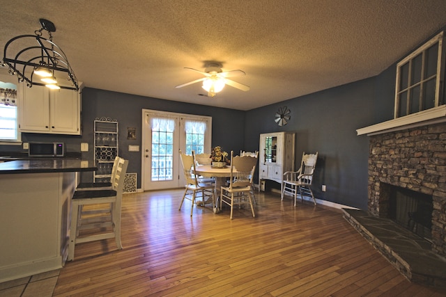 dining area with hardwood / wood-style floors, ceiling fan, a stone fireplace, and a textured ceiling