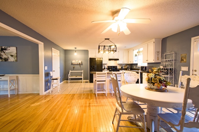 dining area featuring ceiling fan with notable chandelier, light hardwood / wood-style floors, and a textured ceiling