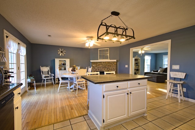 kitchen with a textured ceiling, ceiling fan, white cabinets, black dishwasher, and hanging light fixtures