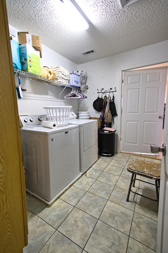 laundry room with washing machine and clothes dryer, light tile patterned floors, and a textured ceiling