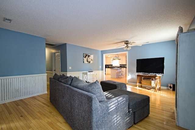 living room with ceiling fan, light wood-type flooring, and a textured ceiling