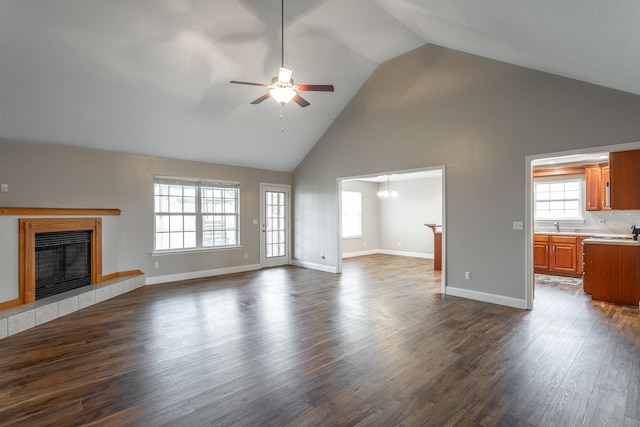 unfurnished living room with ceiling fan with notable chandelier, a wealth of natural light, a tile fireplace, and dark hardwood / wood-style flooring