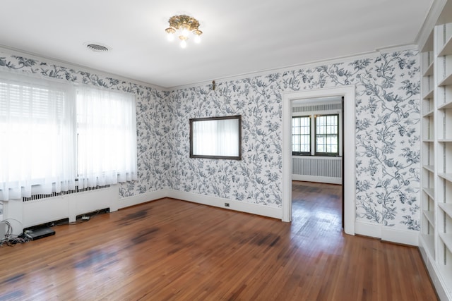 spare room with radiator, crown molding, dark hardwood / wood-style flooring, and built in shelves