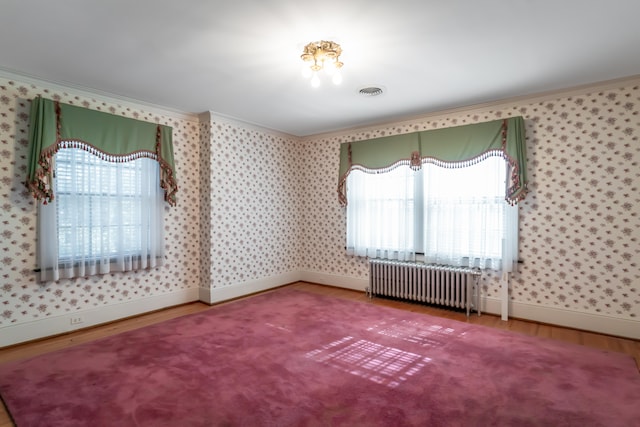 empty room featuring a wealth of natural light, radiator heating unit, ornamental molding, and hardwood / wood-style flooring