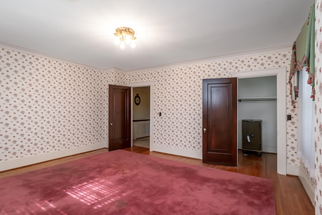 unfurnished bedroom featuring hardwood / wood-style floors, a closet, radiator, and ornamental molding