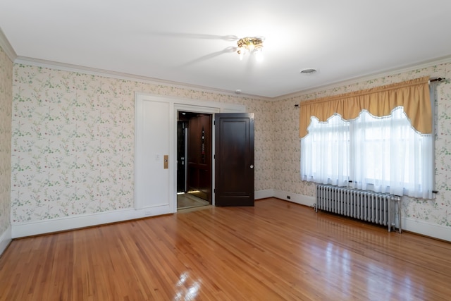 empty room with radiator heating unit, hardwood / wood-style flooring, and ornamental molding