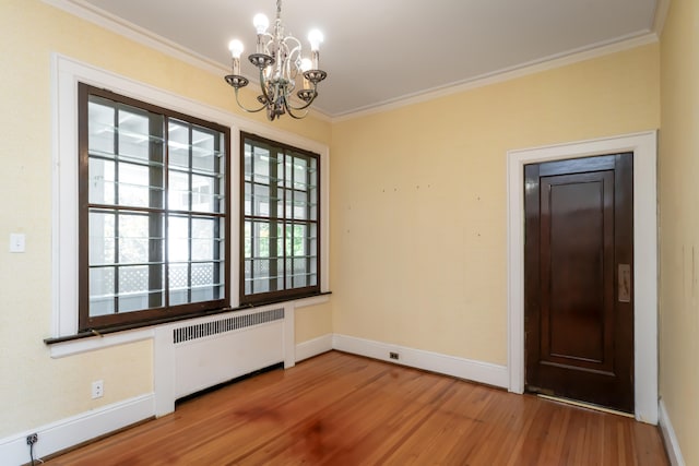 unfurnished dining area with a notable chandelier, wood-type flooring, radiator heating unit, and ornamental molding