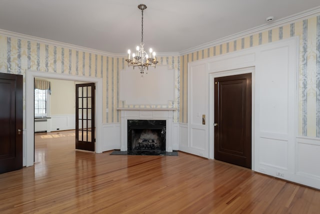 unfurnished living room with crown molding, wood-type flooring, a fireplace, and an inviting chandelier