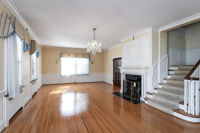 unfurnished living room featuring wood-type flooring, ornamental molding, a high end fireplace, and a chandelier