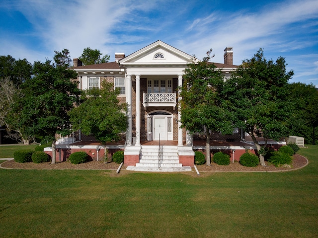 greek revival house featuring a balcony and a front lawn