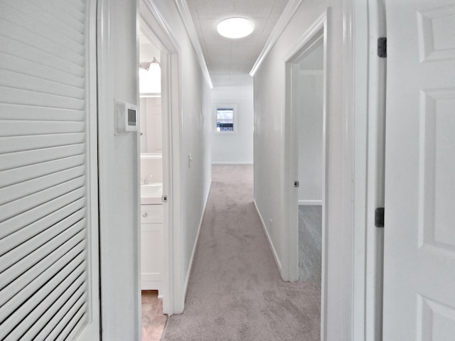 corridor featuring ornamental molding, baseboards, and light carpet