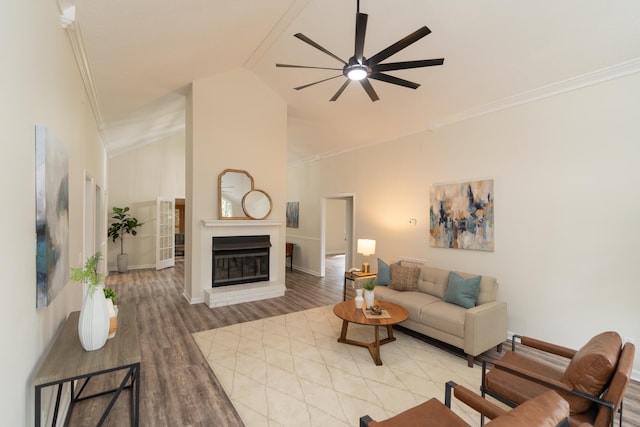 living room with wood-type flooring, a fireplace, ceiling fan, crown molding, and high vaulted ceiling