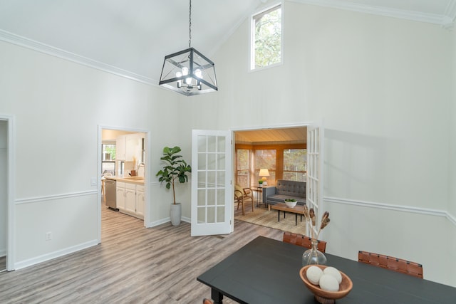 dining space featuring french doors, crown molding, light wood-type flooring, a chandelier, and high vaulted ceiling