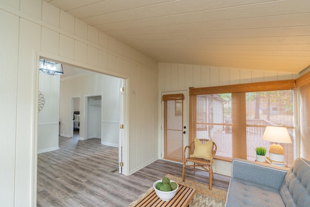 living room with crown molding, wood walls, wood-type flooring, and vaulted ceiling