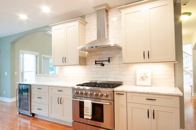 kitchen featuring stainless steel range, wall chimney exhaust hood, wine cooler, and light hardwood / wood-style floors