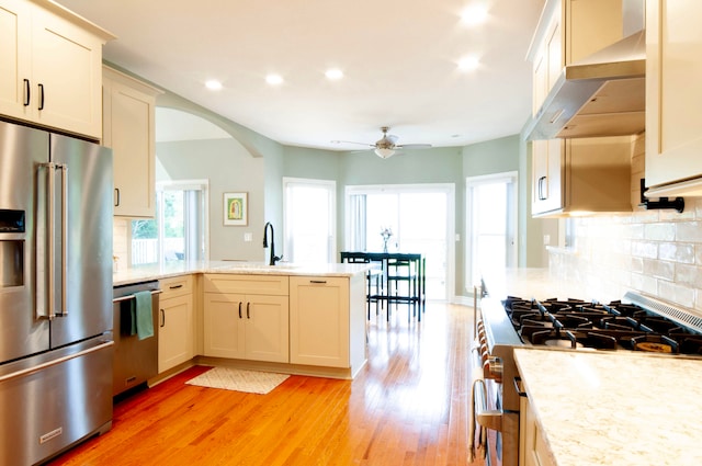 kitchen featuring decorative backsplash, ceiling fan, light hardwood / wood-style flooring, wall chimney exhaust hood, and high end appliances