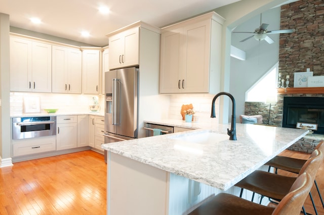 kitchen featuring appliances with stainless steel finishes, light wood-type flooring, kitchen peninsula, white cabinetry, and a breakfast bar area