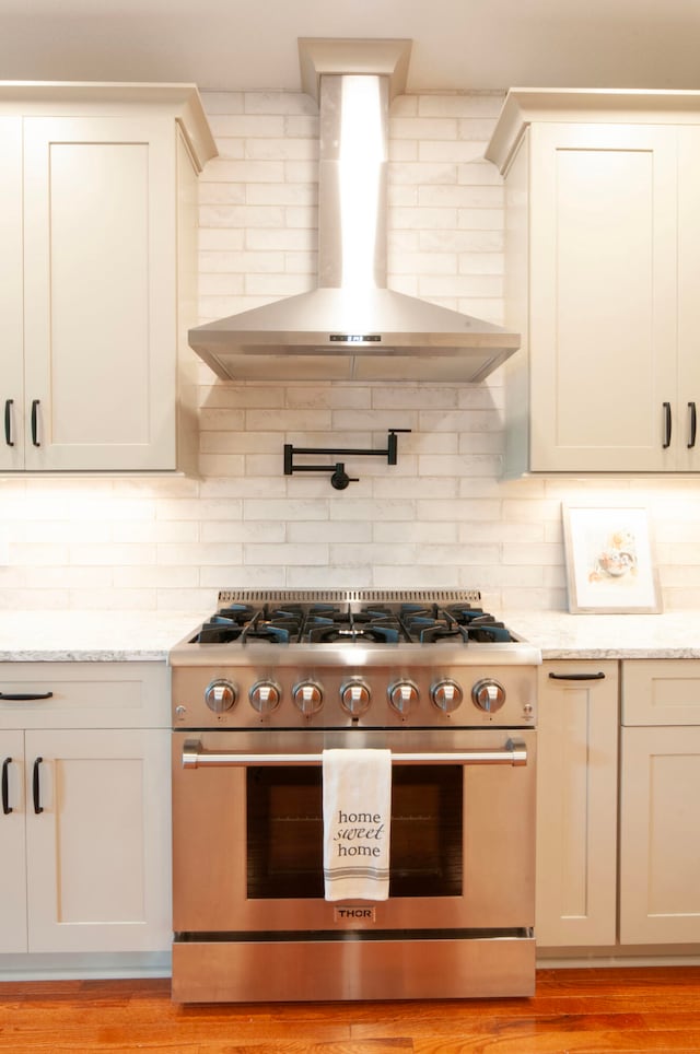 kitchen featuring high end stove, backsplash, light hardwood / wood-style flooring, wall chimney exhaust hood, and light stone counters