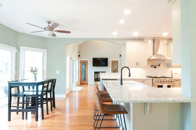 kitchen featuring light hardwood / wood-style flooring, wall chimney range hood, white cabinetry, light stone counters, and a breakfast bar