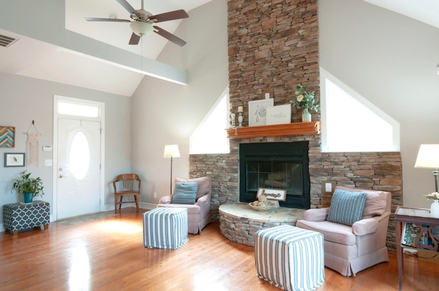 living room featuring light hardwood / wood-style flooring, a stone fireplace, high vaulted ceiling, and ceiling fan