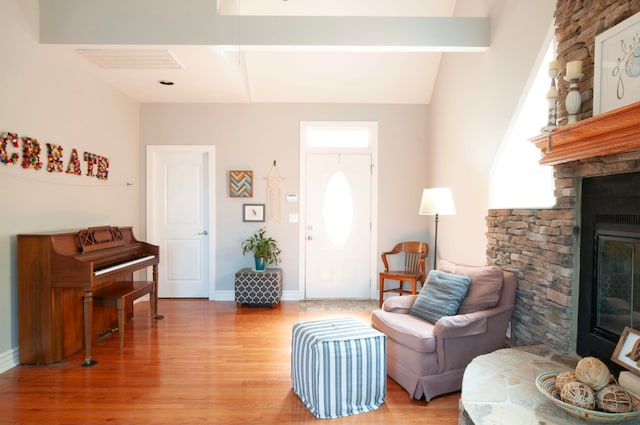 living room with vaulted ceiling with beams, a stone fireplace, and light hardwood / wood-style floors