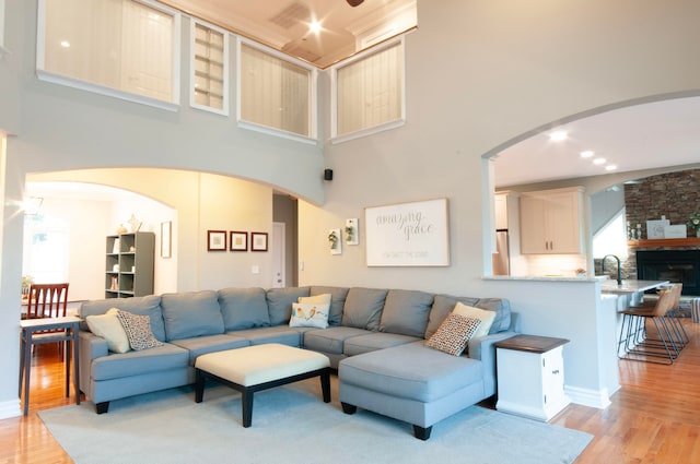 living room featuring a stone fireplace, light hardwood / wood-style flooring, a high ceiling, and a wealth of natural light