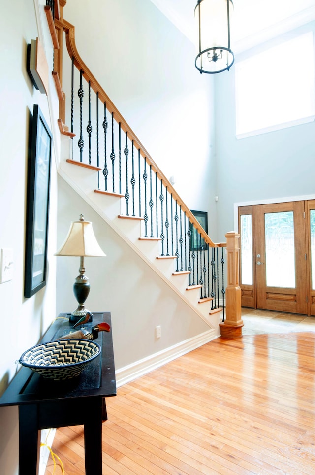 foyer entrance featuring a towering ceiling, wood-type flooring, and a healthy amount of sunlight