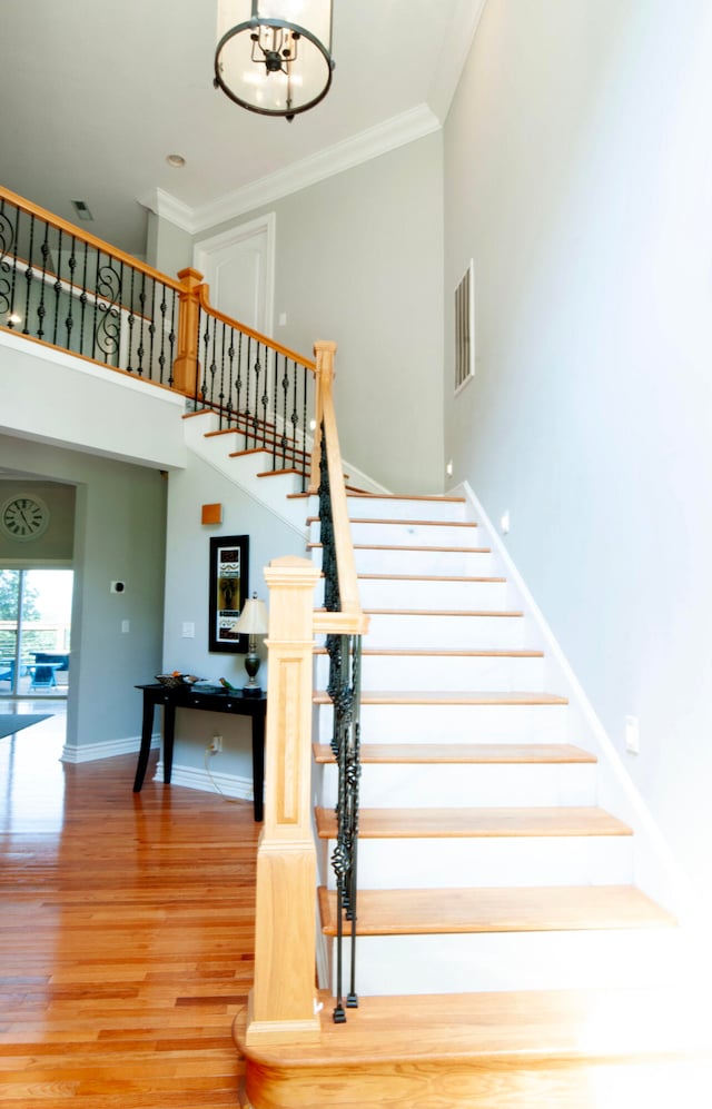 stairs featuring hardwood / wood-style floors, a notable chandelier, crown molding, and a towering ceiling