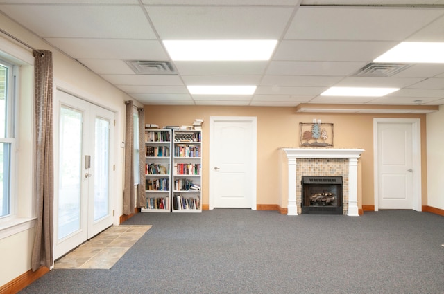 interior space with french doors, a drop ceiling, a brick fireplace, and light colored carpet