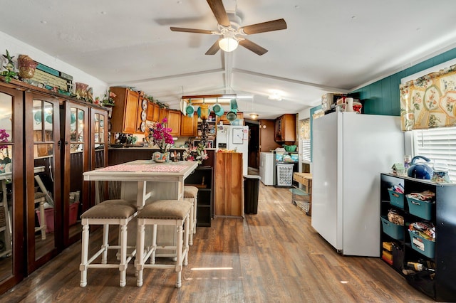 kitchen featuring dark wood-type flooring, a center island, white refrigerator, and a kitchen breakfast bar