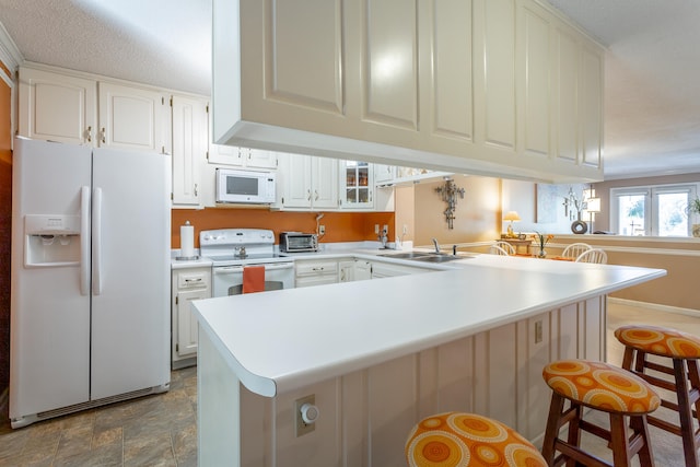 kitchen with kitchen peninsula, white cabinets, a kitchen breakfast bar, sink, and white appliances