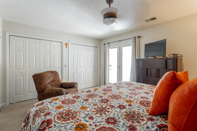 bedroom with multiple closets, a textured ceiling, light colored carpet, and ceiling fan