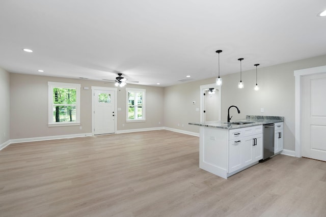 kitchen with light stone counters, decorative light fixtures, open floor plan, white cabinets, and a sink