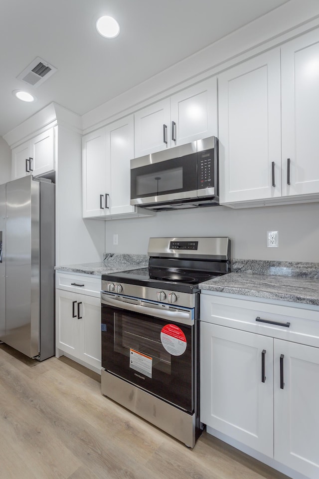 kitchen featuring stainless steel appliances, visible vents, light wood-style floors, and white cabinetry