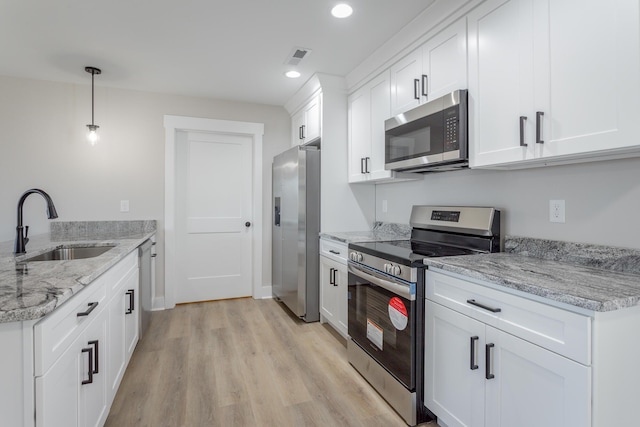 kitchen featuring stainless steel appliances, hanging light fixtures, a sink, and white cabinetry