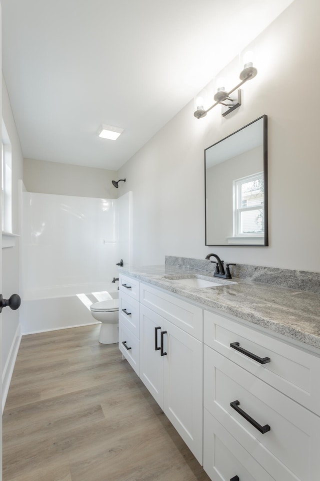 bathroom featuring toilet, tub / shower combination, wood finished floors, and vanity